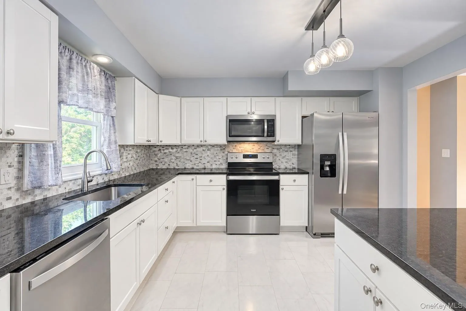Contemporary kitchen showcasing sleek white cabinetry, stainless-steel appliances, and a polished black granite countertop. The mosaic tile backsplash adds texture and visual interest, complemented by light gray walls and large floor tiles for a clean, modern aesthetic. A window above the sink brings in natural light, while pendant lighting over the island provides warmth and sophistication. This kitchen blends functionality and style, ideal for cooking and entertaining. Contemporary kitchen showcasing sleek white cabinetry, stainless-steel appliances, and a polished black granite countertop. The mosaic tile backsplash adds texture and visual interest, complemented by light gray walls and large floor tiles for a clean, modern aesthetic. A window above the sink brings in natural light, while pendant lighting over the island provides warmth and sophistication. This kitchen blends functionality and style, ideal for cooking and entertaining.