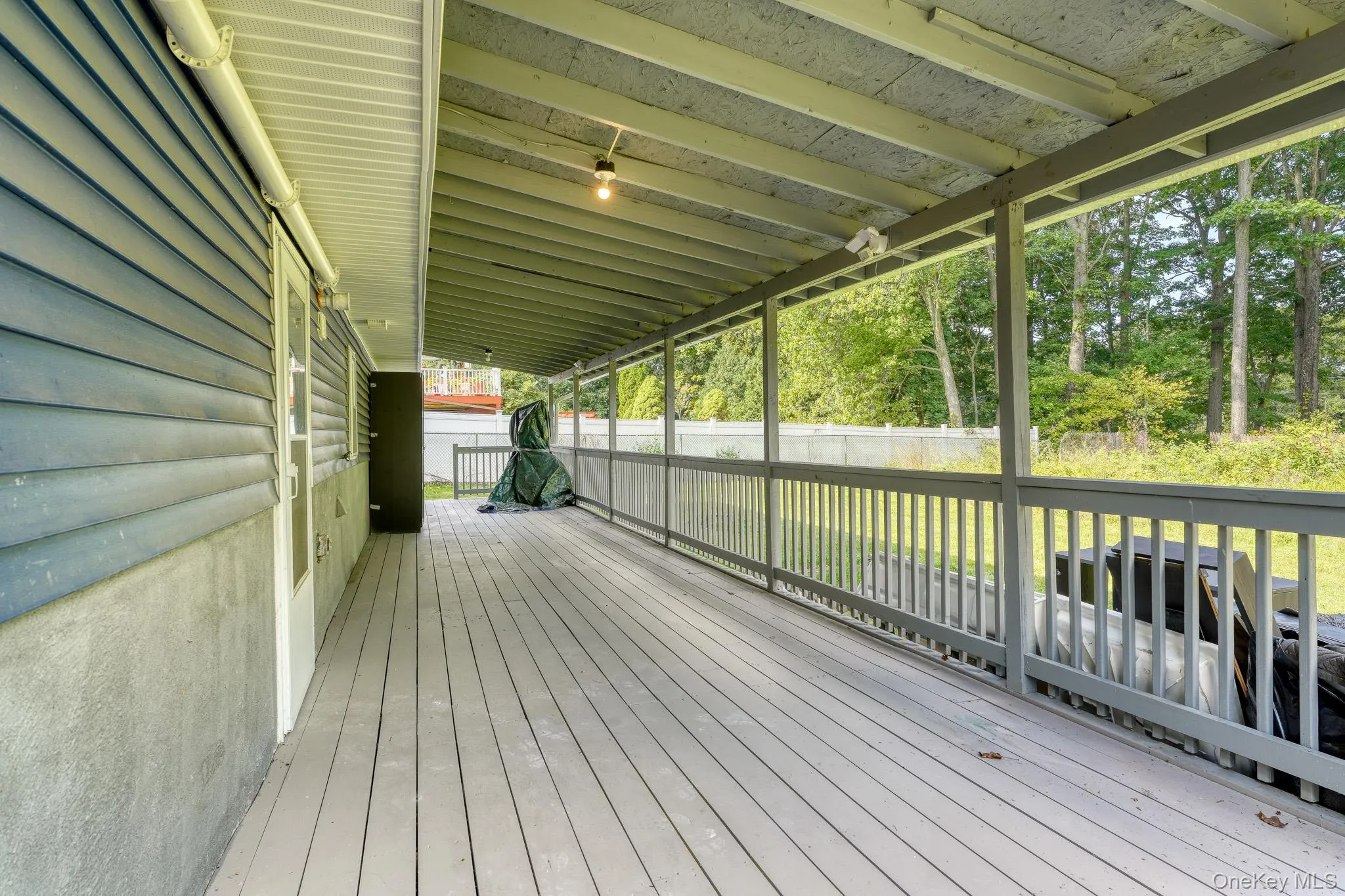 Spacious rear porch featuring a durable wood deck and full overhead coverage for year-round use. The design includes blue siding, white trim, and open railing that frames views of the fenced yard and mature trees beyond. This versatile outdoor area is perfect for gatherings, grilling, or simply unwinding in a private, serene setting. Spacious rear porch featuring a durable wood deck and full overhead coverage for year-round use. The design includes blue siding, white trim, and open railing that frames views of the fenced yard and mature trees beyond. This versatile outdoor area is perfect for gatherings, grilling, or simply unwinding in a private, serene setting.