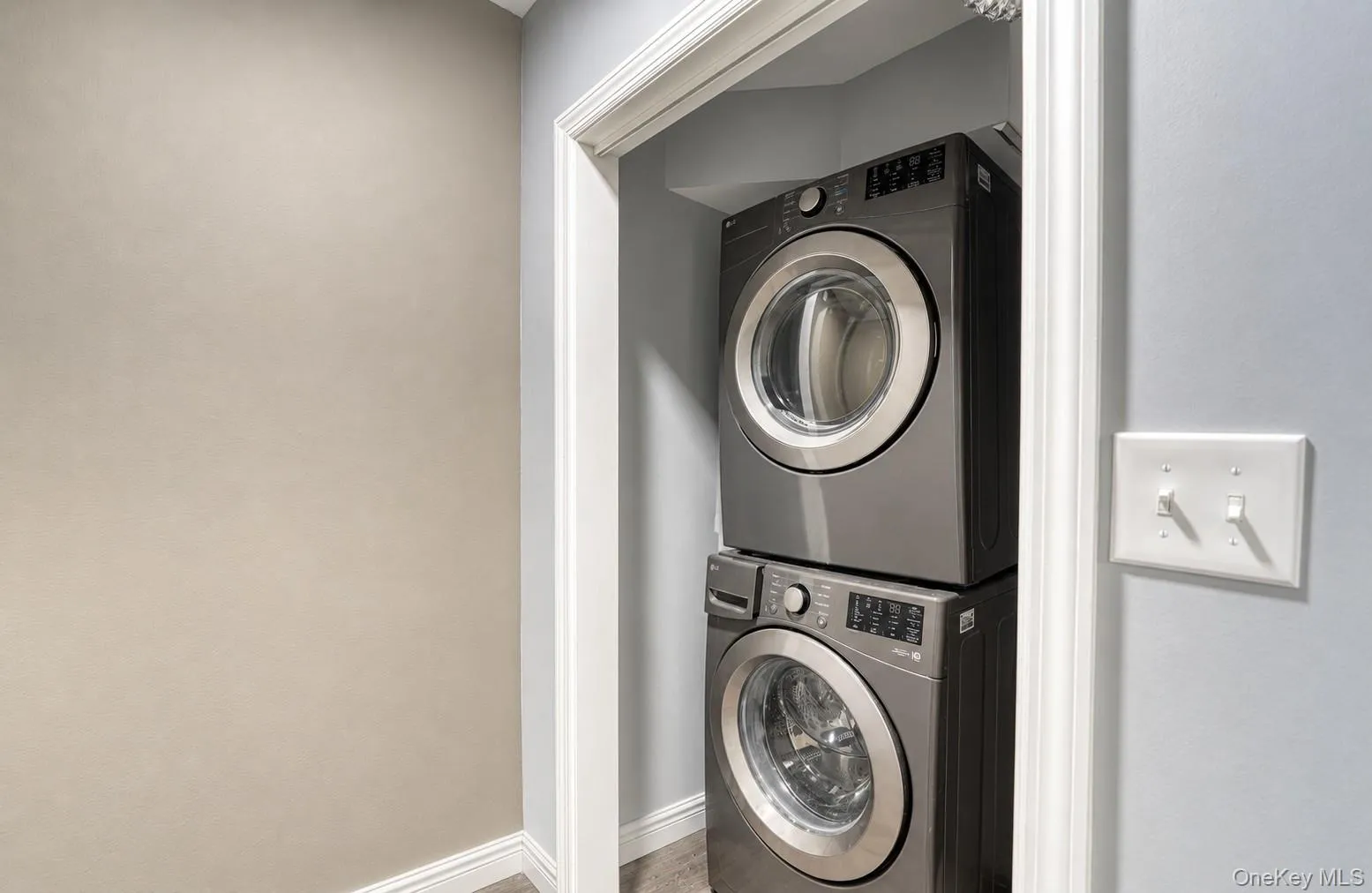 Compact and efficient laundry nook featuring a modern stacked washer and dryer set in a recessed space with clean white trim. The sleek metallic finish of the appliances complements the neutral gray and beige walls, creating a polished, contemporary look. This setup maximizes functionality while maintaining a streamlined aesthetic — perfect for convenient, space-saving laundry access. Compact and efficient laundry nook featuring a modern stacked washer and dryer set in a recessed space with clean white trim. The sleek metallic finish of the appliances complements the neutral gray and beige walls, creating a polished, contemporary look. This setup maximizes functionality while maintaining a streamlined aesthetic — perfect for convenient, space-saving laundry access.