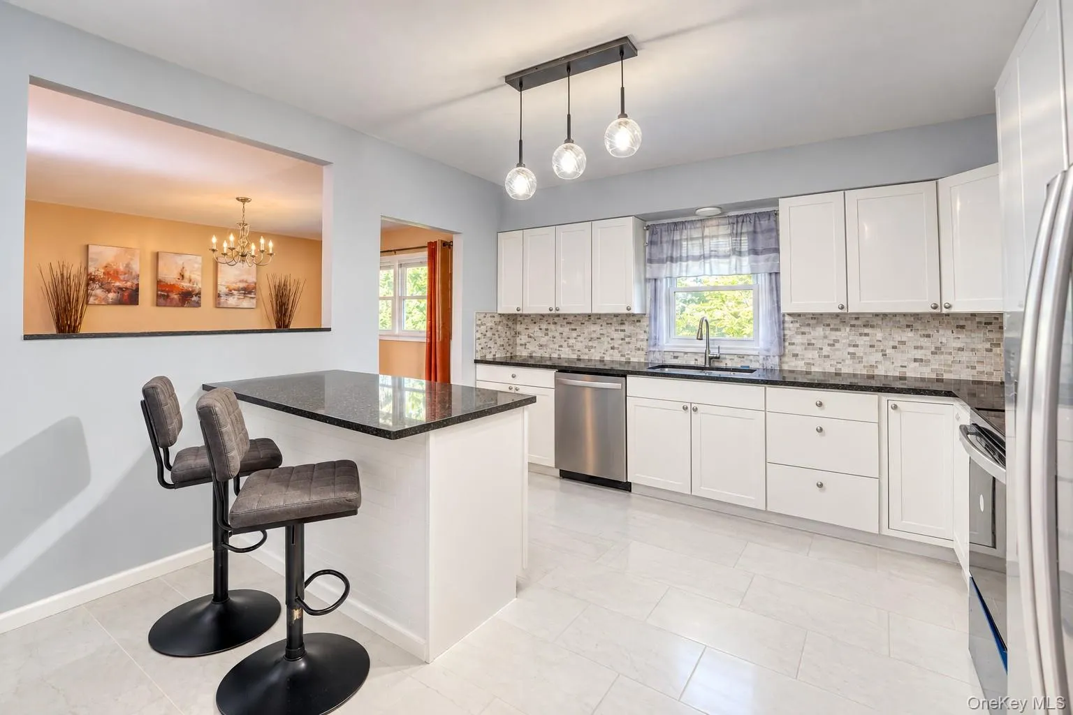 Bright, open kitchen featuring white shaker cabinets, black granite countertops, and a stylish mosaic tile backsplash. A large center island with seating for two creates the perfect spot for casual dining or entertaining. Modern pendant lighting adds a designer touch, while stainless-steel appliances and a window overlooking greenery complete the space. The open pass-through connects seamlessly to the dining area, enhancing flow and natural light throughout. Bright, open kitchen featuring white shaker cabinets, black granite countertops, and a stylish mosaic tile backsplash. A large center island with seating for two creates the perfect spot for casual dining or entertaining. Modern pendant lighting adds a designer touch, while stainless-steel appliances and a window overlooking greenery complete the space. The open pass-through connects seamlessly to the dining area, enhancing flow and natural light throughout.