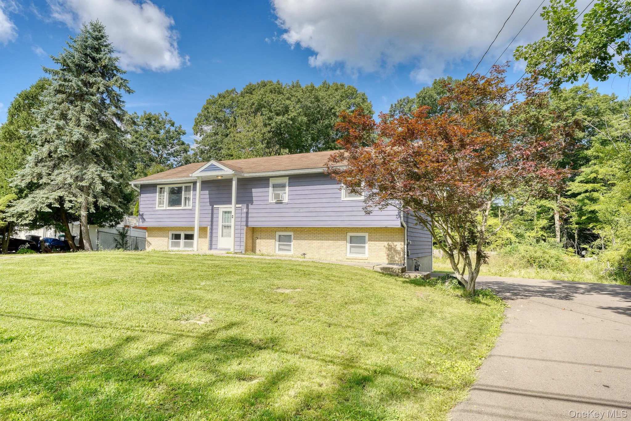 Attractive split-level home with a modern purple exterior and light brick foundation, set on a spacious, well-kept lawn. The front entrance features a small covered portico with white trim and columns, adding a touch of classic charm. Mature trees and a paved driveway frame the property beautifully, while the bright blue sky and lush greenery highlight its inviting curb appeal. Attractive split-level home with a modern purple exterior and light brick foundation, set on a spacious, well-kept lawn. The front entrance features a small covered portico with white trim and columns, adding a touch of classic charm. Mature trees and a paved driveway frame the property beautifully, while the bright blue sky and lush greenery highlight its inviting curb appeal.