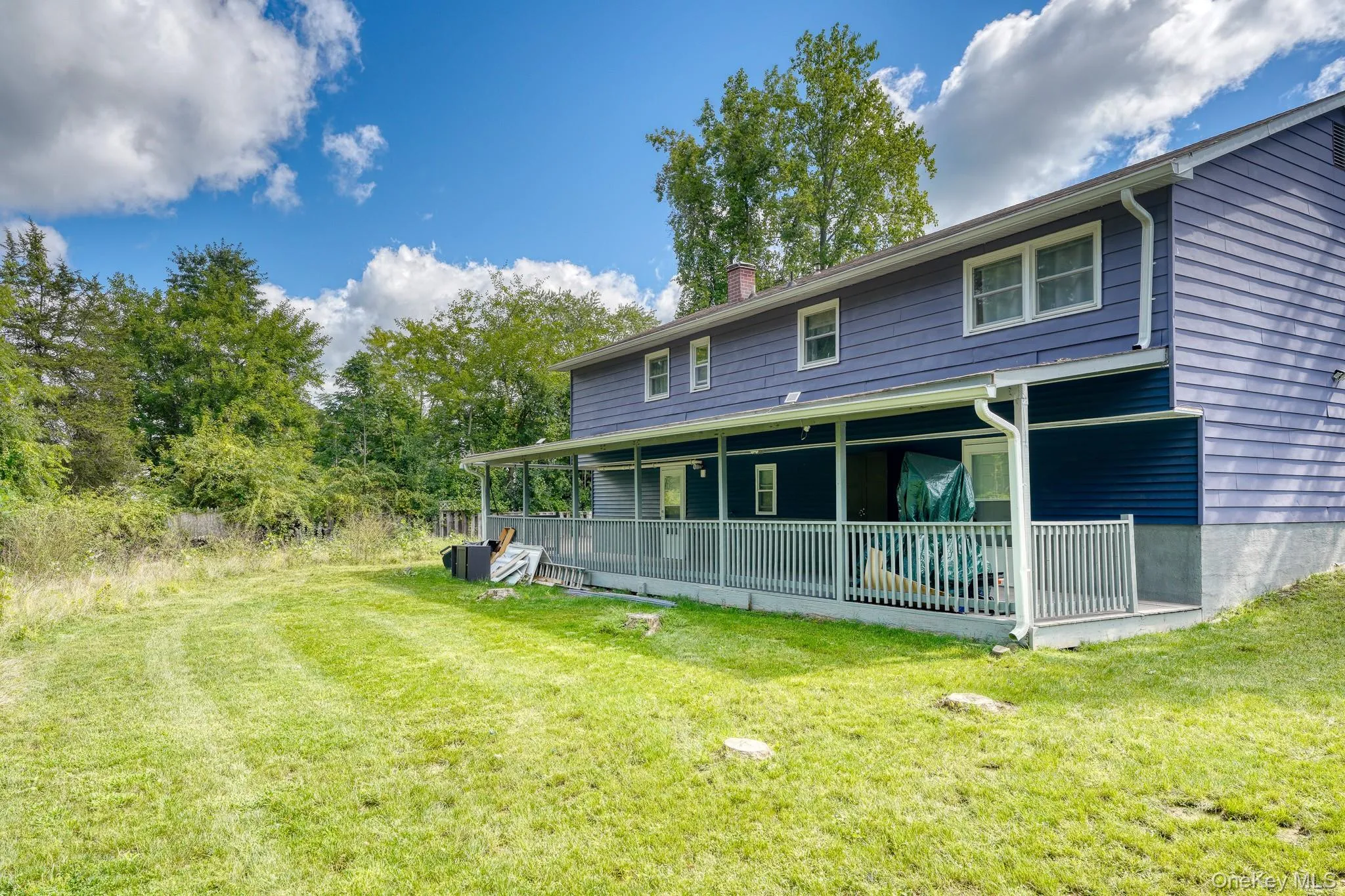 Expansive backyard featuring a large, covered porch that spans the length of the home — perfect for outdoor relaxation or entertaining. The home’s blue siding and white trim create a crisp, modern look against the lush green lawn and wooded backdrop. With plenty of open space and privacy, this yard offers endless potential for gardening, recreation, or future enhancements. Expansive backyard featuring a large, covered porch that spans the length of the home — perfect for outdoor relaxation or entertaining. The home’s blue siding and white trim create a crisp, modern look against the lush green lawn and wooded backdrop. With plenty of open space and privacy, this yard offers endless potential for gardening, recreation, or future enhancements.