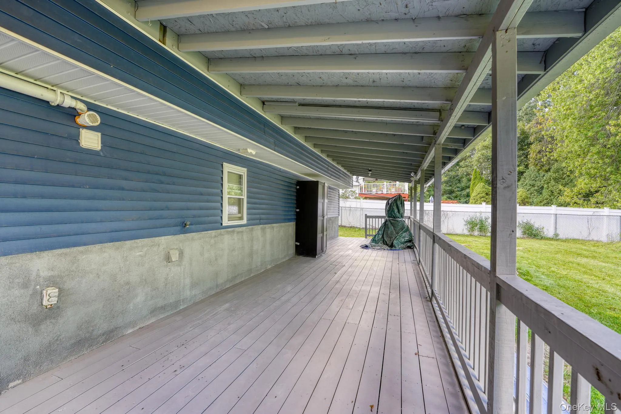 Expansive covered back porch with light gray decking and sturdy railing, offering a shaded retreat overlooking the backyard. The blue siding and exposed beams add a touch of rustic charm, while the open layout provides plenty of space for outdoor seating or storage. Ideal for relaxing, entertaining, or enjoying peaceful views of the surrounding greenery. Expansive covered back porch with light gray decking and sturdy railing, offering a shaded retreat overlooking the backyard. The blue siding and exposed beams add a touch of rustic charm, while the open layout provides plenty of space for outdoor seating or storage. Ideal for relaxing, entertaining, or enjoying peaceful views of the surrounding greenery.
