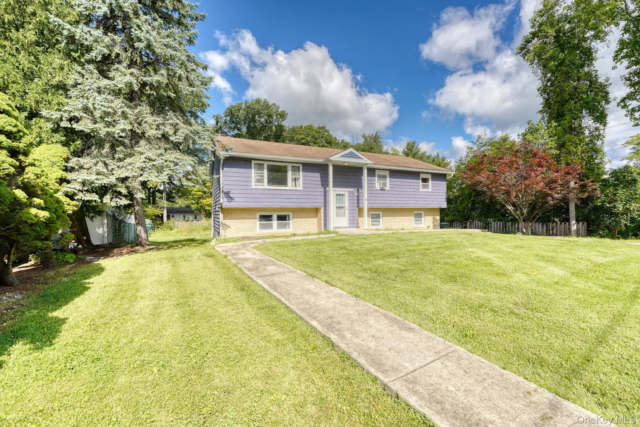 Charming split-level home with a welcoming front entrance and manicured lawn. The exterior combines light brickwork with blue siding for a modern yet classic look. A concrete walkway leads to the front door framed by a small gable, while mature trees and landscaped greenery add curb appeal. Bright and inviting, this front view showcases the property’s spacious lot and peaceful suburban setting. Charming split-level home with a welcoming front entrance and manicured lawn. The exterior combines light brickwork with blue siding for a modern yet classic look. A concrete walkway leads to the front door framed by a small gable, while mature trees and landscaped greenery add curb appeal. Bright and inviting, this front view showcases the property’s spacious lot and peaceful suburban setting.
