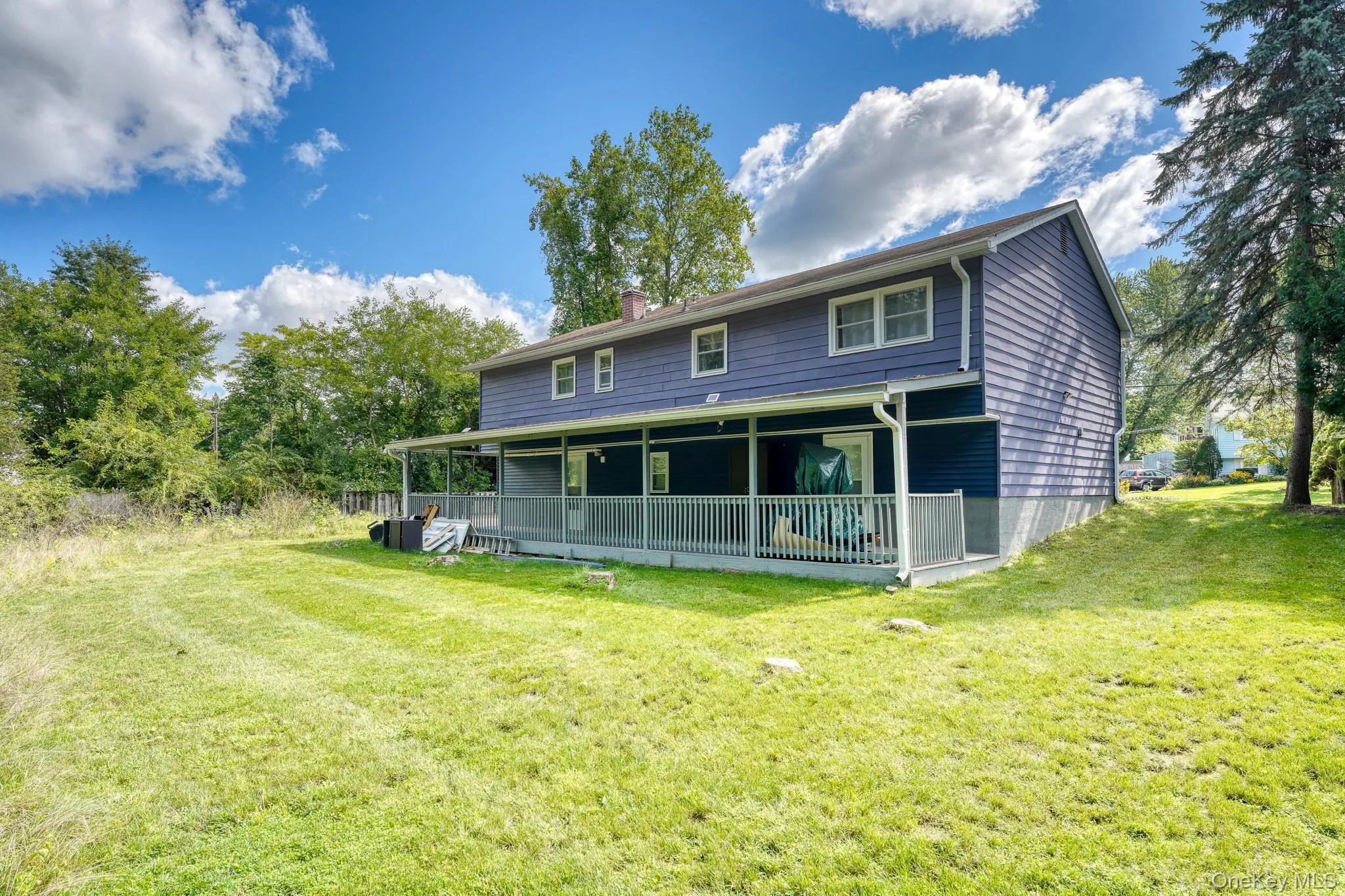 Beautiful outdoor setting showcasing a spacious lawn and a two-story home with a full-length covered porch. The blue exterior contrasts elegantly with the surrounding greenery and bright sky, creating a serene, inviting atmosphere. Ideal for gatherings or quiet evenings outdoors, this backyard combines natural beauty with functional space for year-round enjoyment. Beautiful outdoor setting showcasing a spacious lawn and a two-story home with a full-length covered porch. The blue exterior contrasts elegantly with the surrounding greenery and bright sky, creating a serene, inviting atmosphere. Ideal for gatherings or quiet evenings outdoors, this backyard combines natural beauty with functional space for year-round enjoyment.