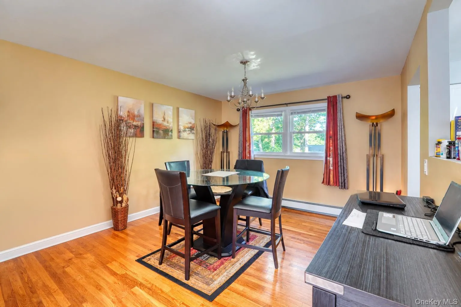 Bright, contemporary dining space with polished hardwood floors and a cozy, open layout. The room centers around a round glass-top table with dark wood seating, complemented by warm tan walls and abstract artwork. Large windows with patterned curtains bring in abundant natural light, while stylish floor lamps and a chandelier create an upscale yet comfortable atmosphere — perfect for family meals or gatherings. Bright, contemporary dining space with polished hardwood floors and a cozy, open layout. The room centers around a round glass-top table with dark wood seating, complemented by warm tan walls and abstract artwork. Large windows with patterned curtains bring in abundant natural light, while stylish floor lamps and a chandelier create an upscale yet comfortable atmosphere — perfect for family meals or gatherings.