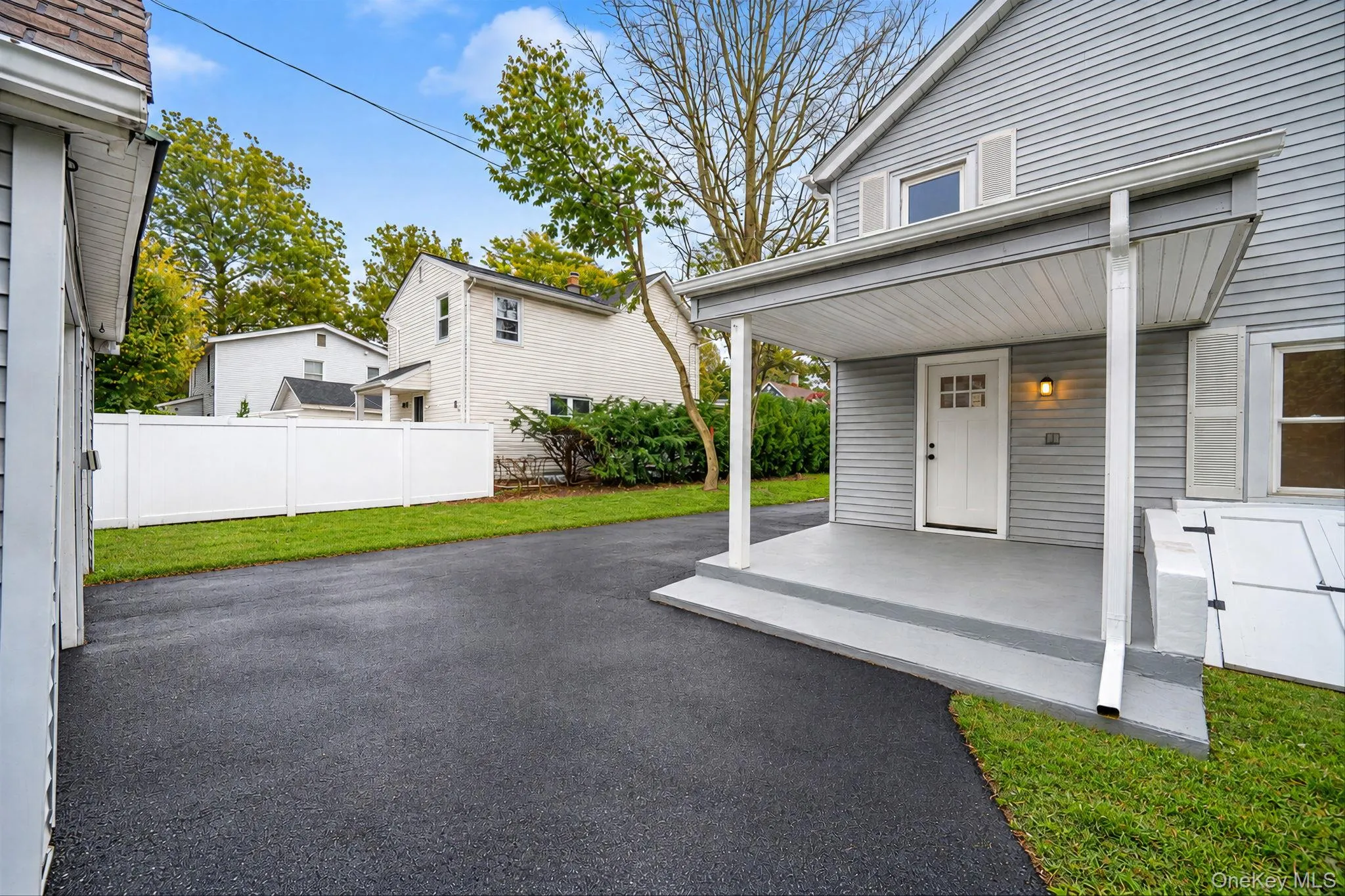 Exterior featuring horizontal siding, a covered porch with concrete flooring, an asphalt driveway, and a white privacy fence Exterior featuring horizontal siding, a covered porch with concrete flooring, an asphalt driveway, and a white privacy fence