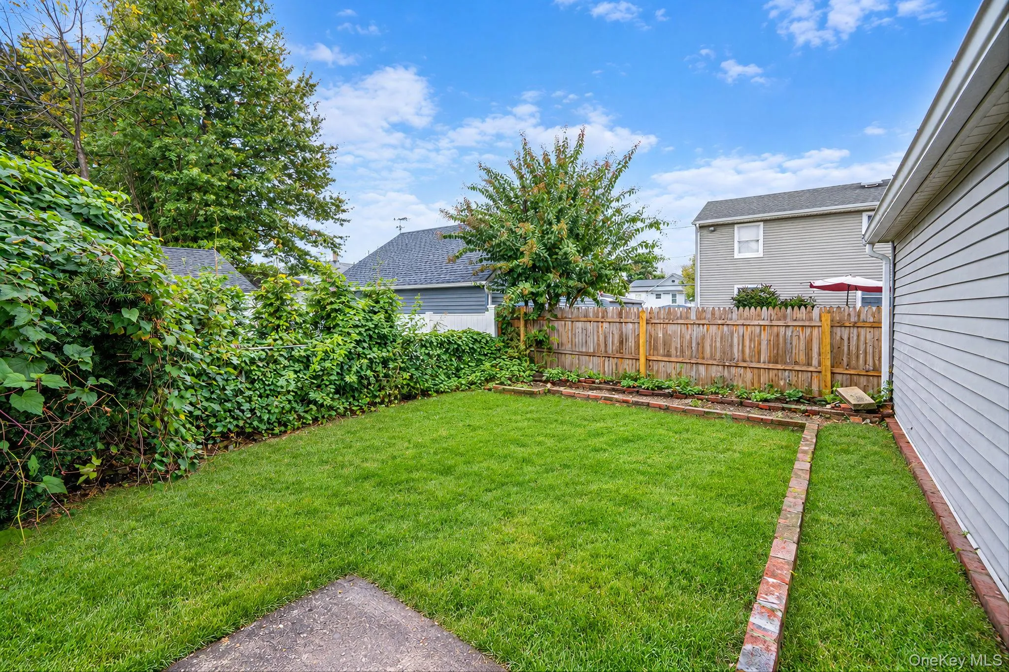 Private backyard featuring a fenced perimeter, brick-edged garden beds, and mature landscaping *virtually edited Private backyard featuring a fenced perimeter, brick-edged garden beds, and mature landscaping *virtually edited