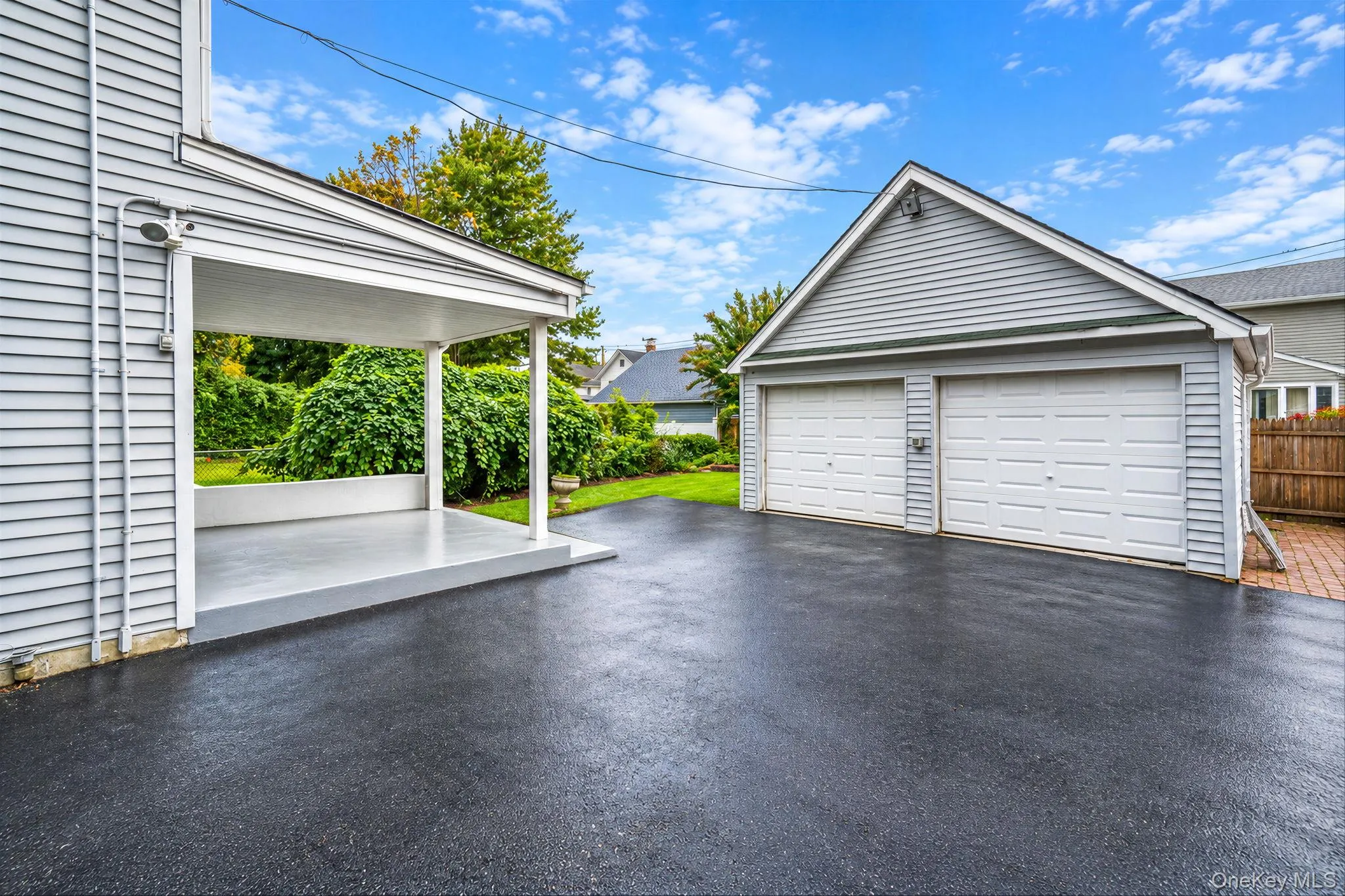 Exterior space featuring a covered patio, two-car detached garage with white overhead doors, and asphalt driveway Exterior space featuring a covered patio, two-car detached garage with white overhead doors, and asphalt driveway