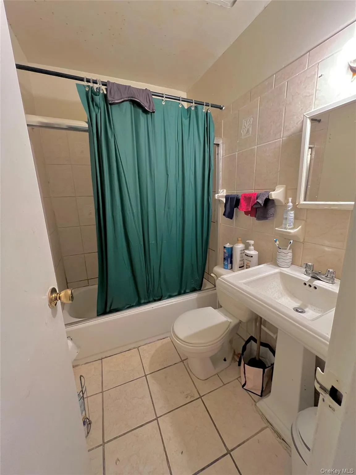 Full bathroom featuring toilet, shower / bath combination with curtain, tile walls, tile patterned flooring, and tasteful backsplash Full bathroom featuring toilet, shower / bath combination with curtain, tile walls, tile patterned flooring, and tasteful backsplash