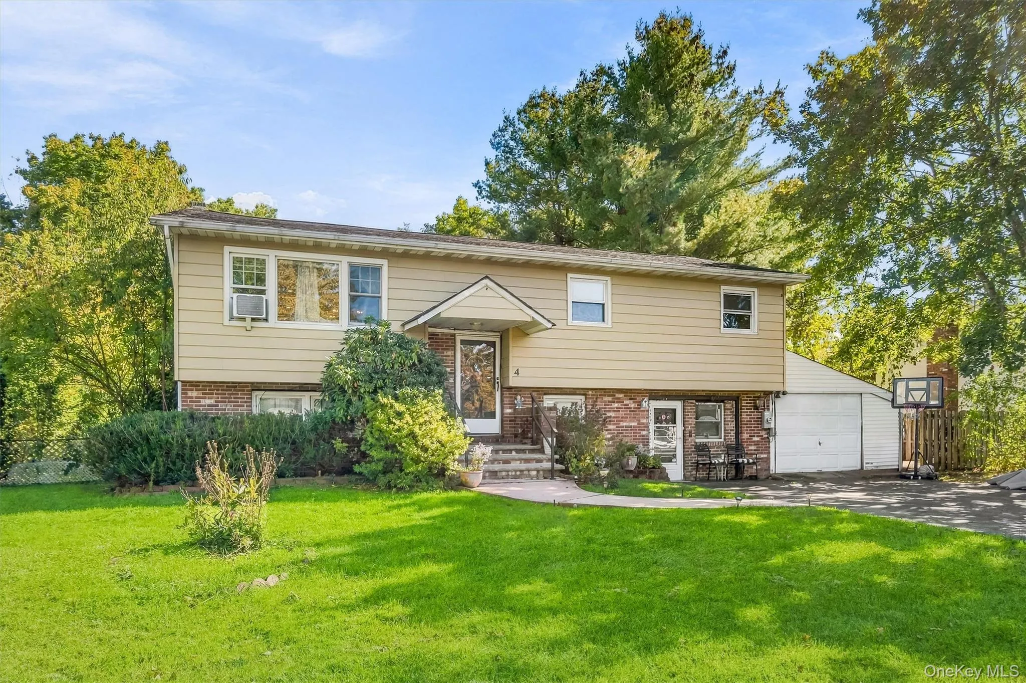 Split-level exterior featuring tan horizontal siding, a red brick base, covered entryway with a gabled roof, and an attached single-car garage Split-level exterior featuring tan horizontal siding, a red brick base, covered entryway with a gabled roof, and an attached single-car garage