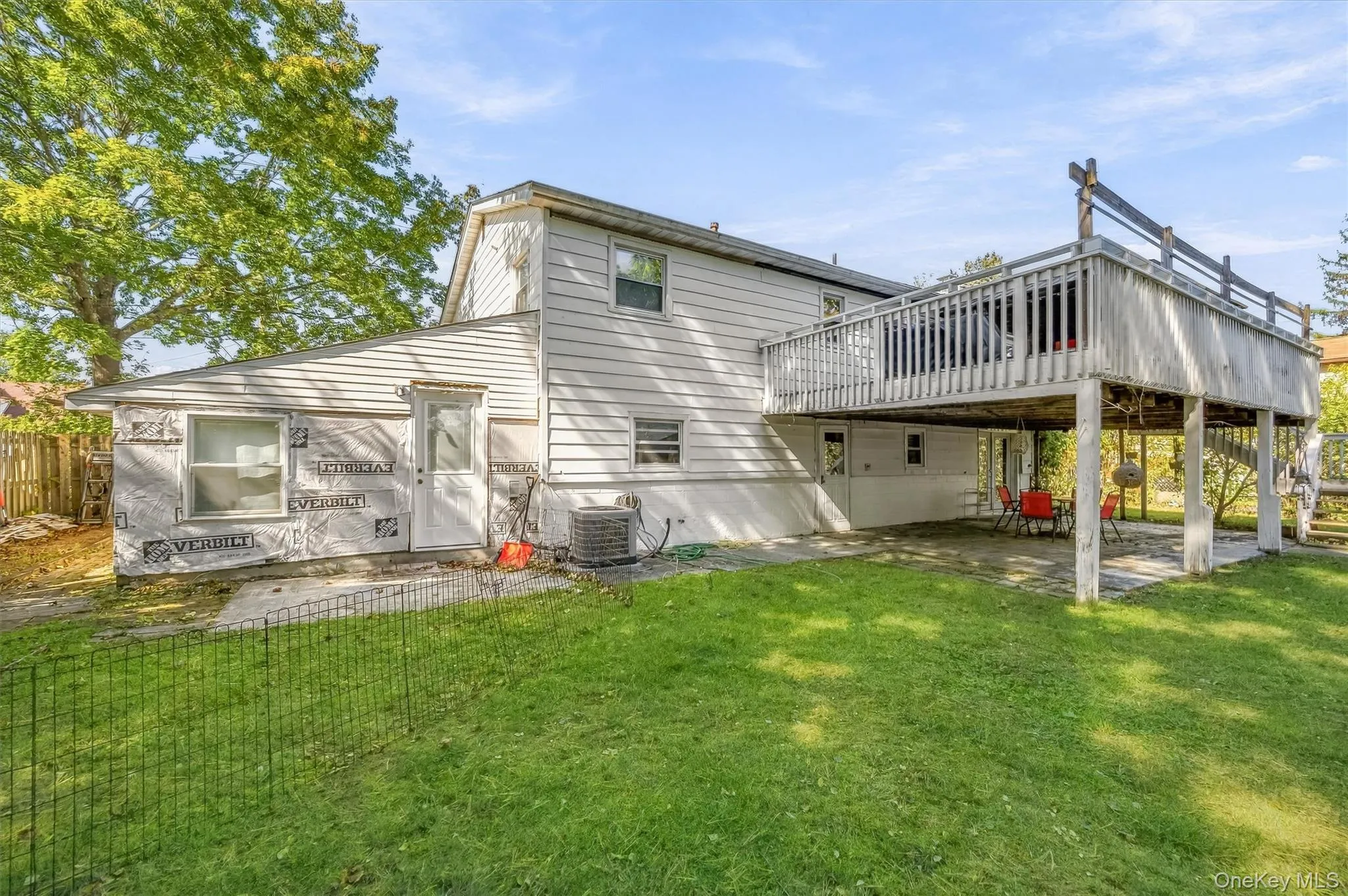 Exterior featuring light-colored horizontal siding, a raised deck with perimeter railing, a concrete patio, and a grass lawn Exterior featuring light-colored horizontal siding, a raised deck with perimeter railing, a concrete patio, and a grass lawn