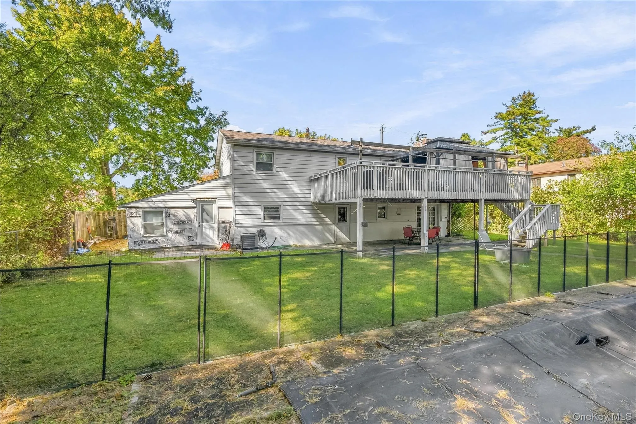 Rear exterior featuring a raised wooden deck with staircase, ground-level paved patio, fenced backyard, and siding Rear exterior featuring a raised wooden deck with staircase, ground-level paved patio, fenced backyard, and siding