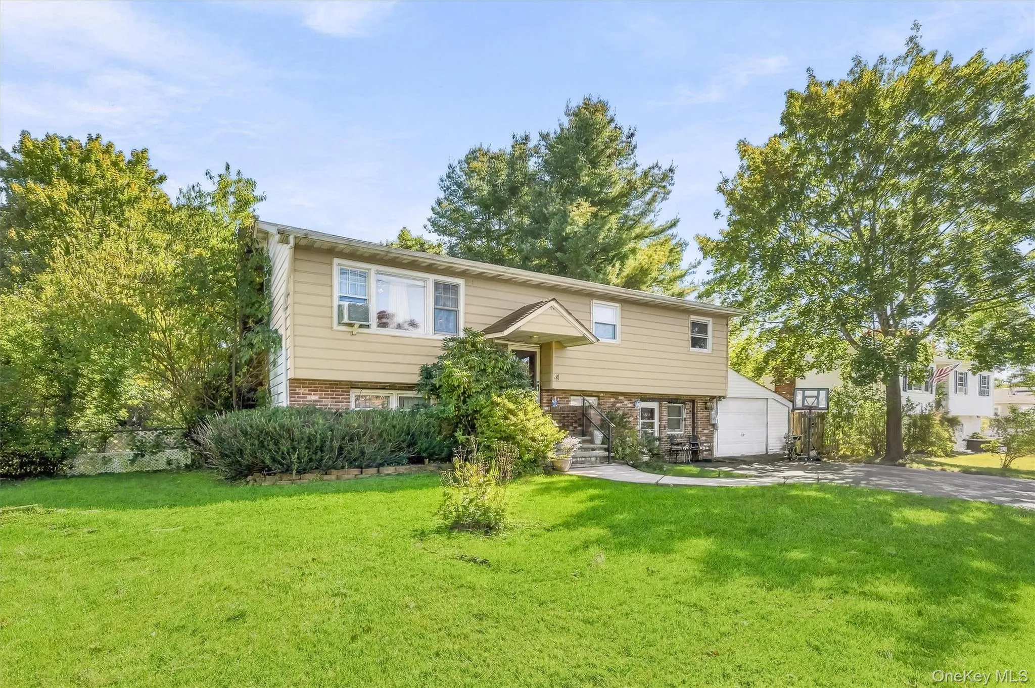 Split-level exterior featuring tan siding, brick masonry, a covered entryway, and an attached garage Split-level exterior featuring tan siding, brick masonry, a covered entryway, and an attached garage
