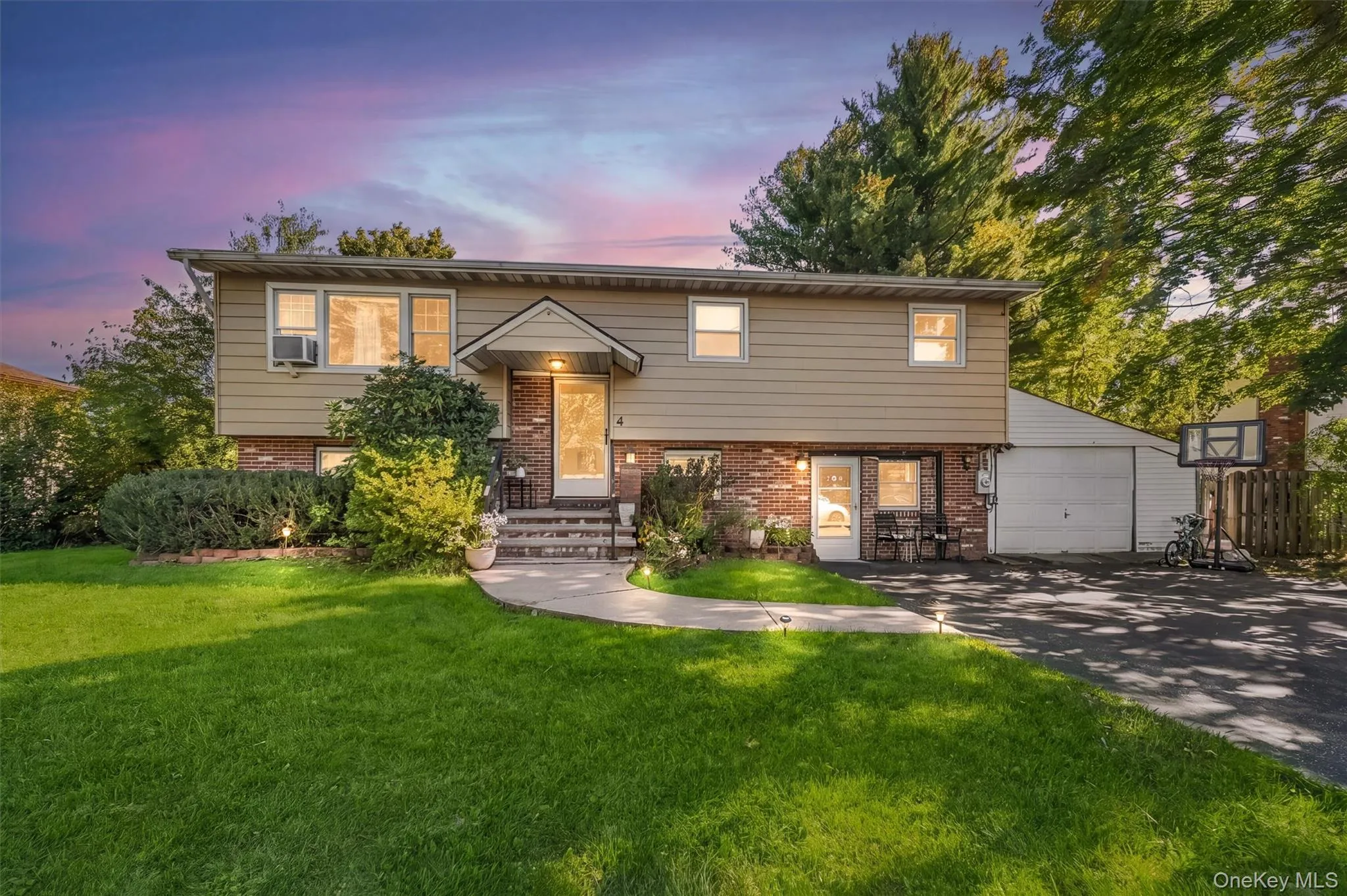 Split-level exterior featuring a brick and horizontal siding facade, a covered front entryway, attached one-car garage, and concrete walkway Split-level exterior featuring a brick and horizontal siding facade, a covered front entryway, attached one-car garage, and concrete walkway