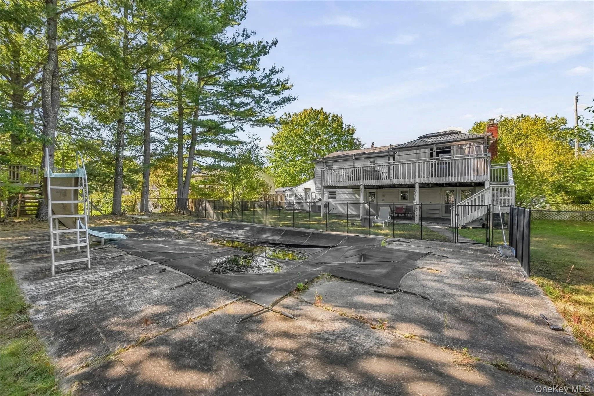 Outdoor pool with slide, concrete patio, multi-level deck, and mature trees Outdoor pool with slide, concrete patio, multi-level deck, and mature trees