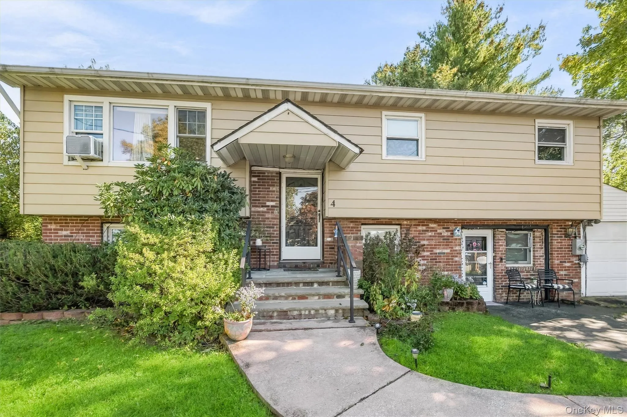 Split-level exterior featuring a brick and horizontal siding facade, a covered front entryway, concrete walkway, and attached garage Split-level exterior featuring a brick and horizontal siding facade, a covered front entryway, concrete walkway, and attached garage