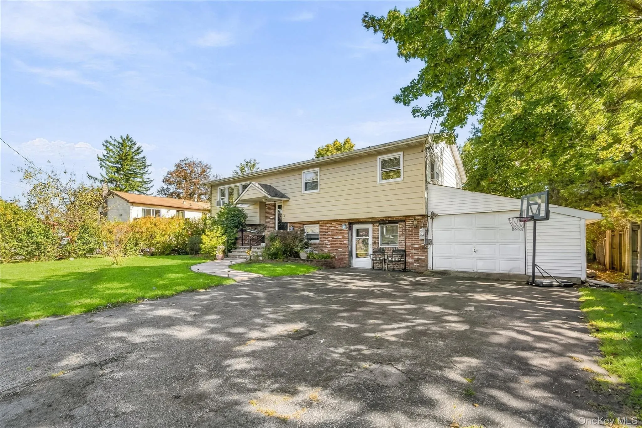 Split-level exterior featuring light horizontal siding, partial brick facade, attached garage, and paved driveway Split-level exterior featuring light horizontal siding, partial brick facade, attached garage, and paved driveway