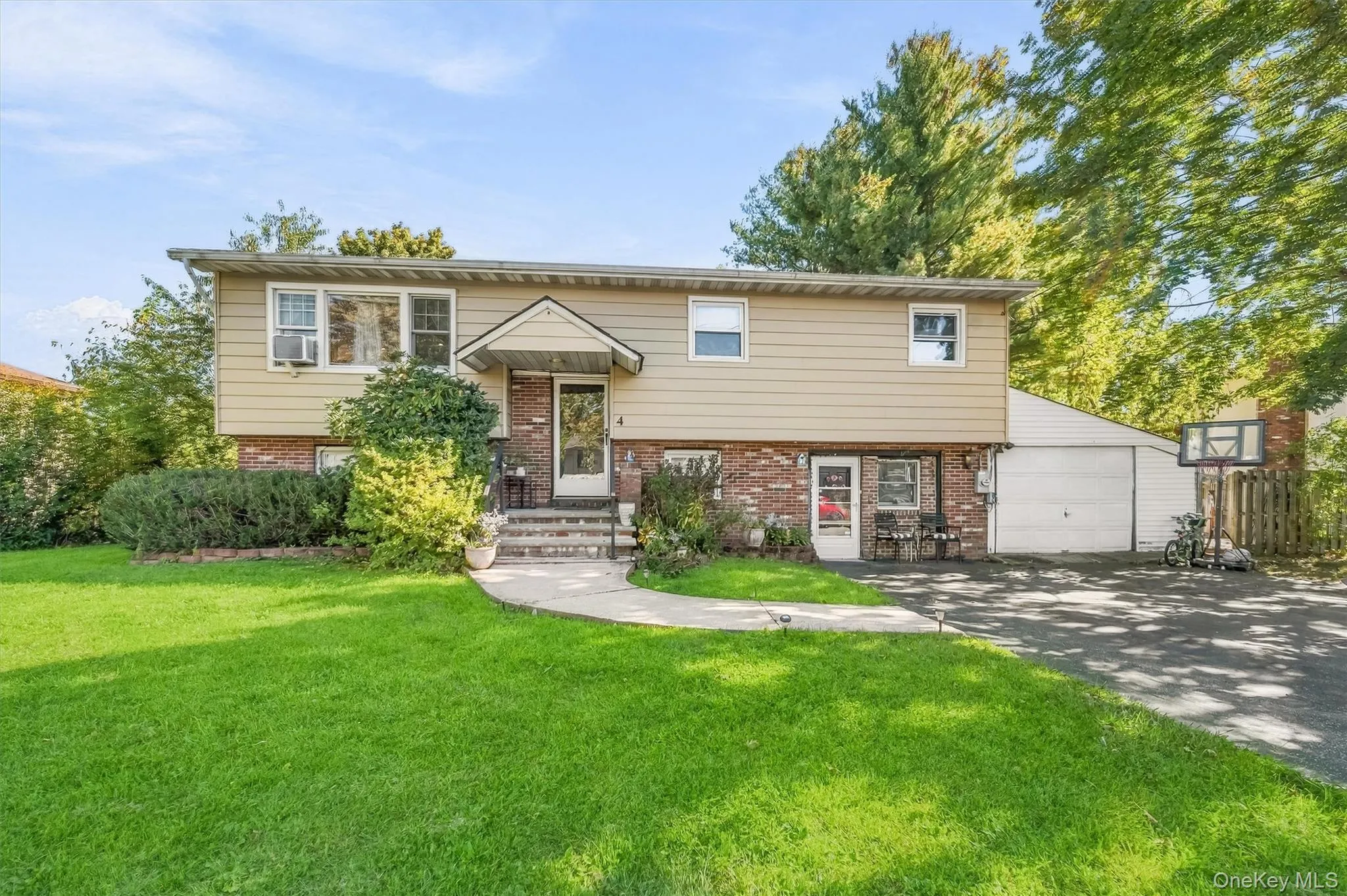 Split-level exterior featuring a brick and horizontal siding facade, a covered entryway, an attached garage, and a concrete walkway Split-level exterior featuring a brick and horizontal siding facade, a covered entryway, an attached garage, and a concrete walkway