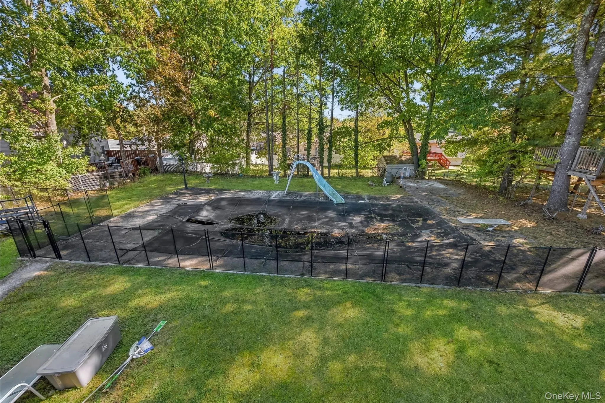 Rear yard featuring an in-ground pool with a surrounding metal safety fence, a poolside slide, and mature perimeter trees Rear yard featuring an in-ground pool with a surrounding metal safety fence, a poolside slide, and mature perimeter trees