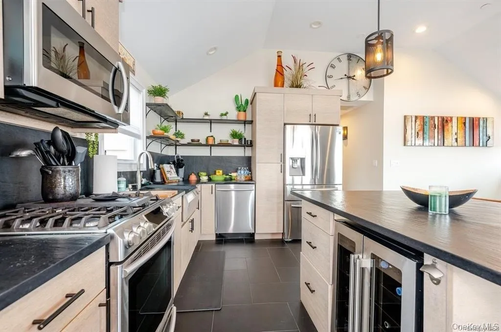 Kitchen featuring open shelves, stainless steel appliances, beverage cooler, vaulted ceiling, and decorative light fixtures Kitchen featuring open shelves, stainless steel appliances, beverage cooler, vaulted ceiling, and decorative light fixtures
