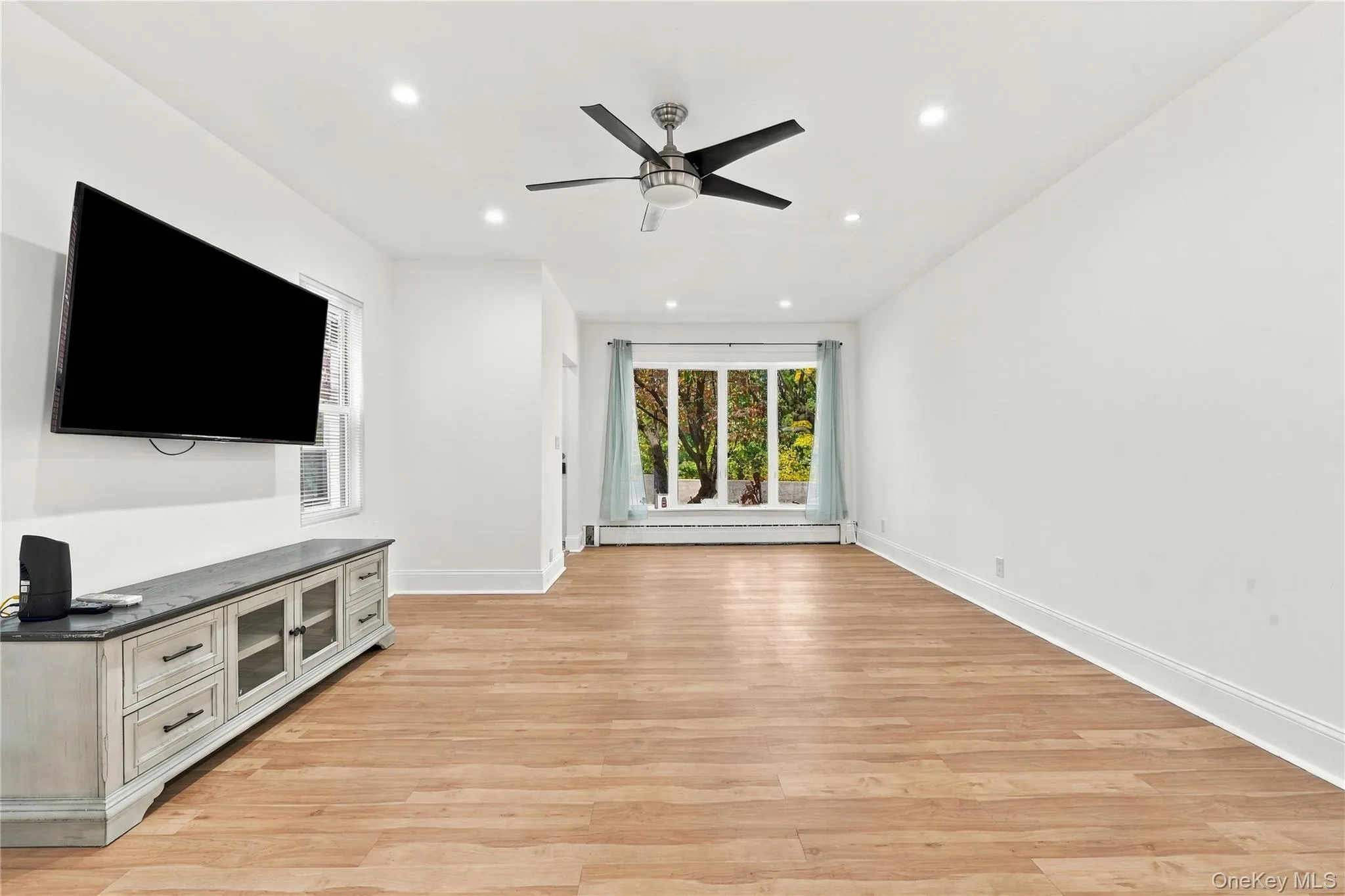 Interior space featuring wood-finish flooring, recessed lighting, a ceiling fan, and a large bay window Interior space featuring wood-finish flooring, recessed lighting, a ceiling fan, and a large bay window