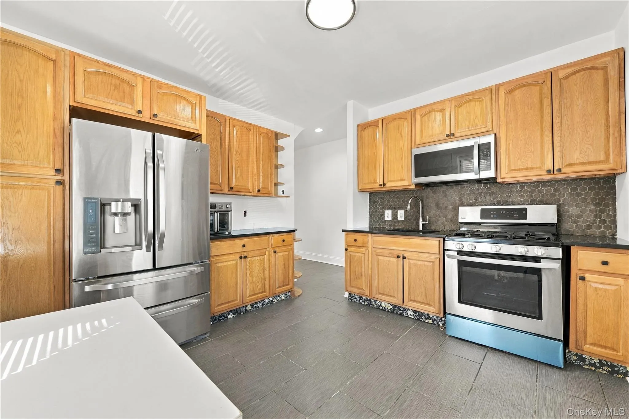 Kitchen featuring wood cabinetry, stainless steel appliances, dark stone-finish countertops, geometric tile backsplash Kitchen featuring wood cabinetry, stainless steel appliances, dark stone-finish countertops, geometric tile backsplash