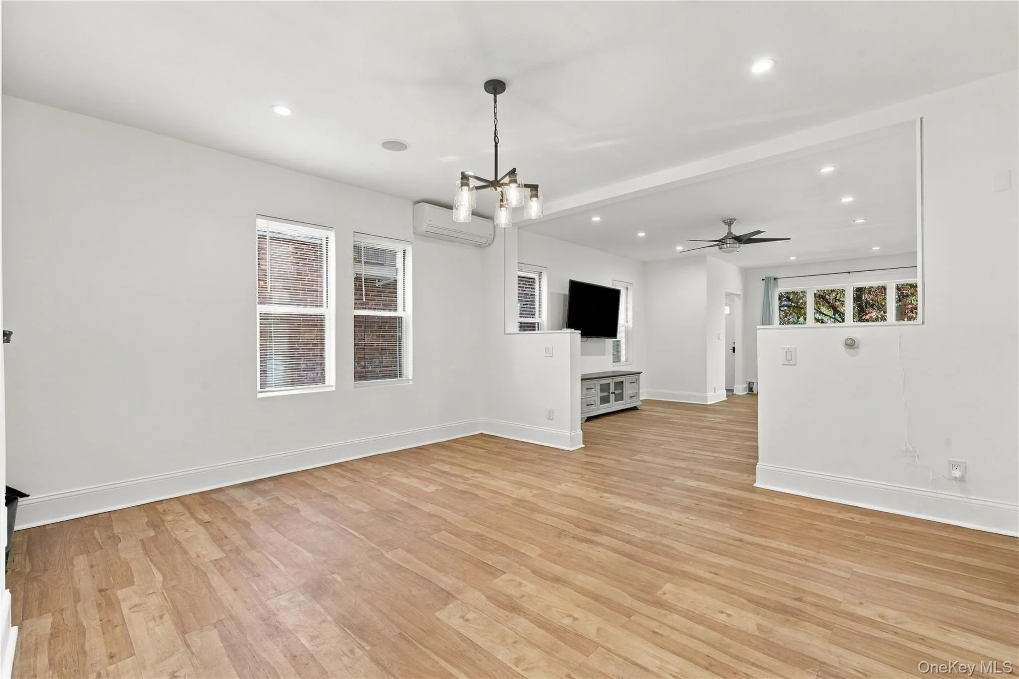 Interior space featuring wood-finish flooring, recessed lighting, a multi-arm chandelier, and a wall-mounted ductless climate control unit Interior space featuring wood-finish flooring, recessed lighting, a multi-arm chandelier, and a wall-mounted ductless climate control unit