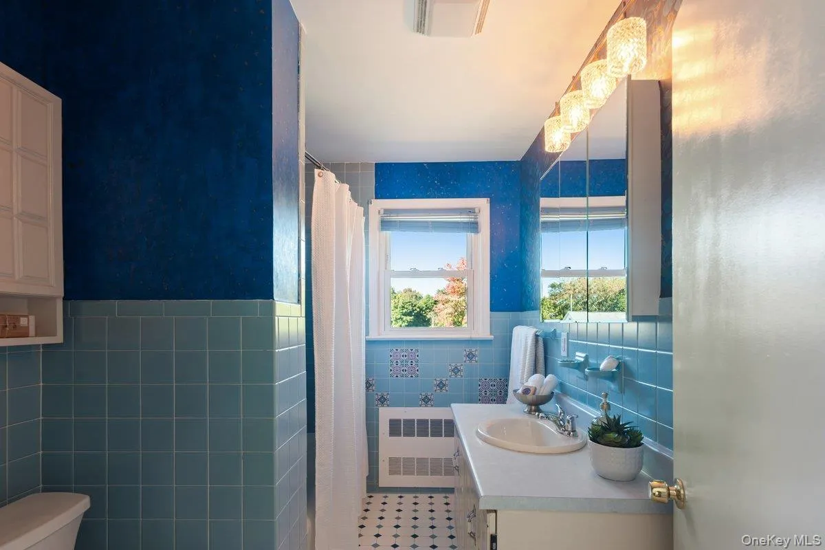 The full hall bath features a window with backyard views, a tub-shower combination, novelty tiles, a large vanity, and new lighting. The full hall bath features a window with backyard views, a tub-shower combination, novelty tiles, a large vanity, and new lighting.