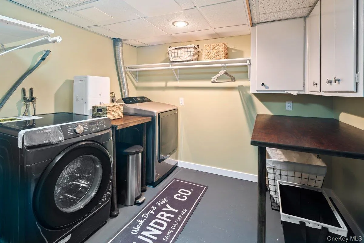 The new laundry area is located in the basement and features a Samsung washer and dryer, folding tables, storage cabinets, and shelves with hanging rods. The new laundry area is located in the basement and features a Samsung washer and dryer, folding tables, storage cabinets, and shelves with hanging rods.
