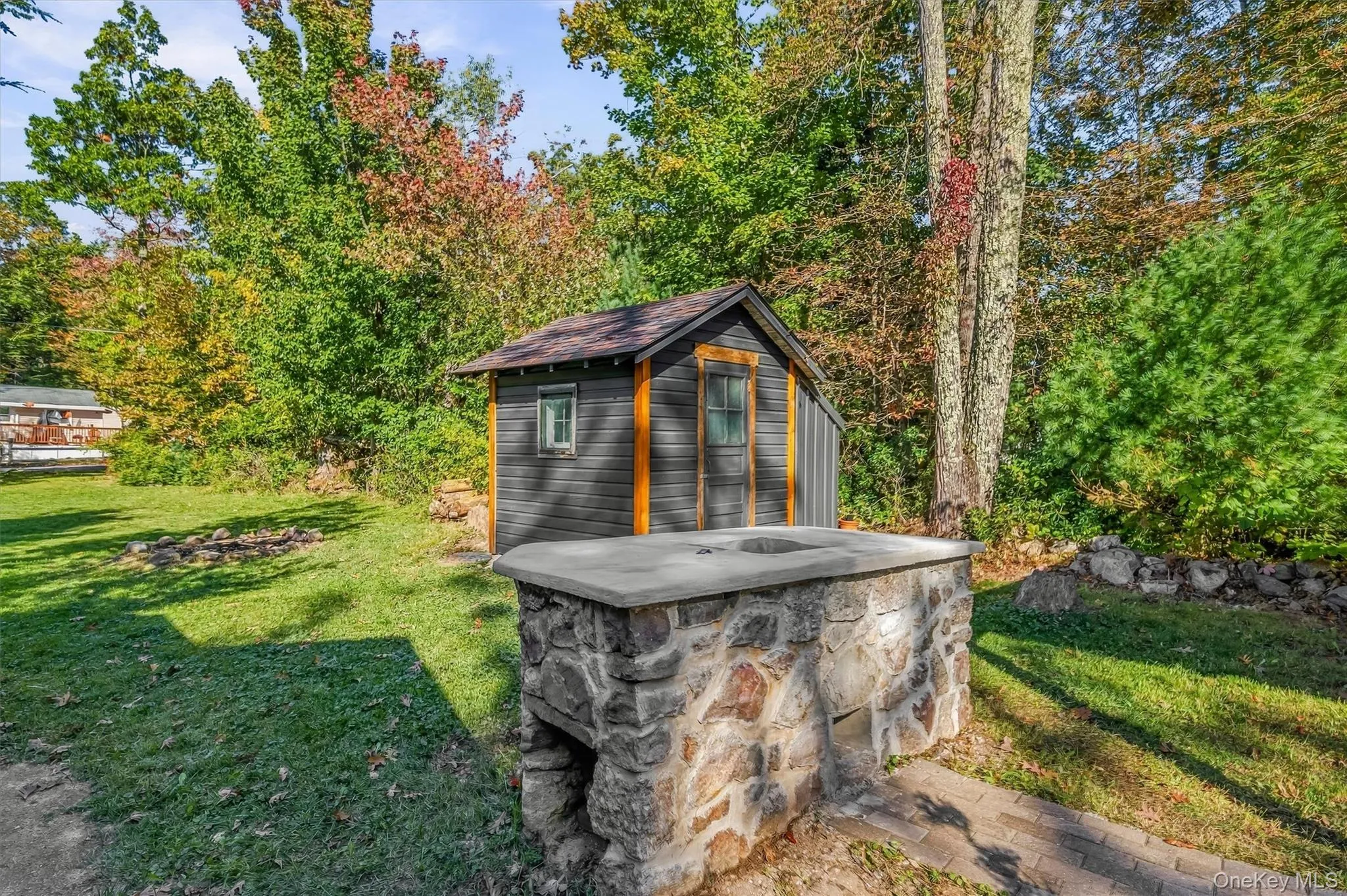 Spacious outdoor area featuring a stone-clad outdoor cooking station, a detached utility shed, a manicured lawn, and mature trees Spacious outdoor area featuring a stone-clad outdoor cooking station, a detached utility shed, a manicured lawn, and mature trees