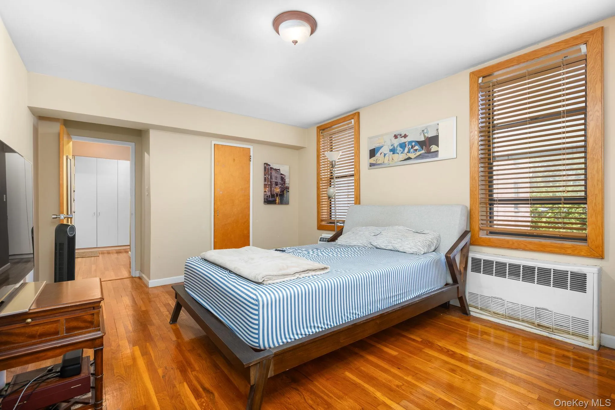 Hardwood flooring throughout, two windows with wood-frame trim, recessed doorway, and a ceiling-mounted light fixture Hardwood flooring throughout, two windows with wood-frame trim, recessed doorway, and a ceiling-mounted light fixture