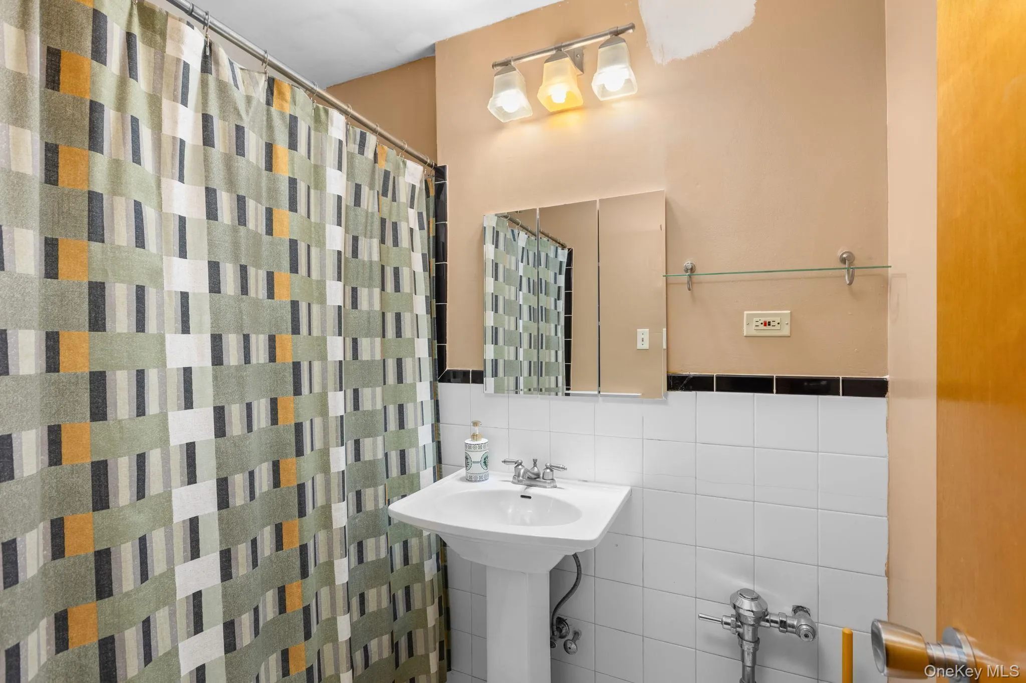 Pedestal sink with chrome faucet, wall-mounted mirror, overhead vanity lighting, and white subway tile surround Pedestal sink with chrome faucet, wall-mounted mirror, overhead vanity lighting, and white subway tile surround