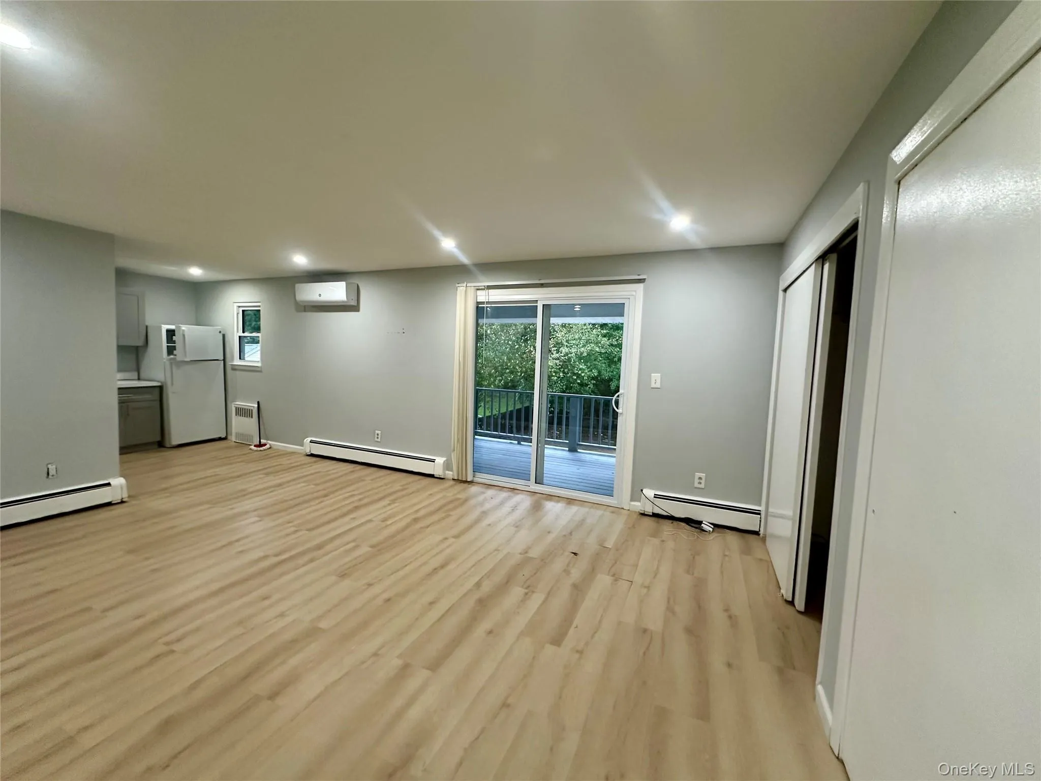 Open-concept interior featuring light wood-finish flooring, recessed lighting, sliding glass door, wall-mounted climate control unit, and closet with sliding doors Open-concept interior featuring light wood-finish flooring, recessed lighting, sliding glass door, wall-mounted climate control unit, and closet with sliding doors