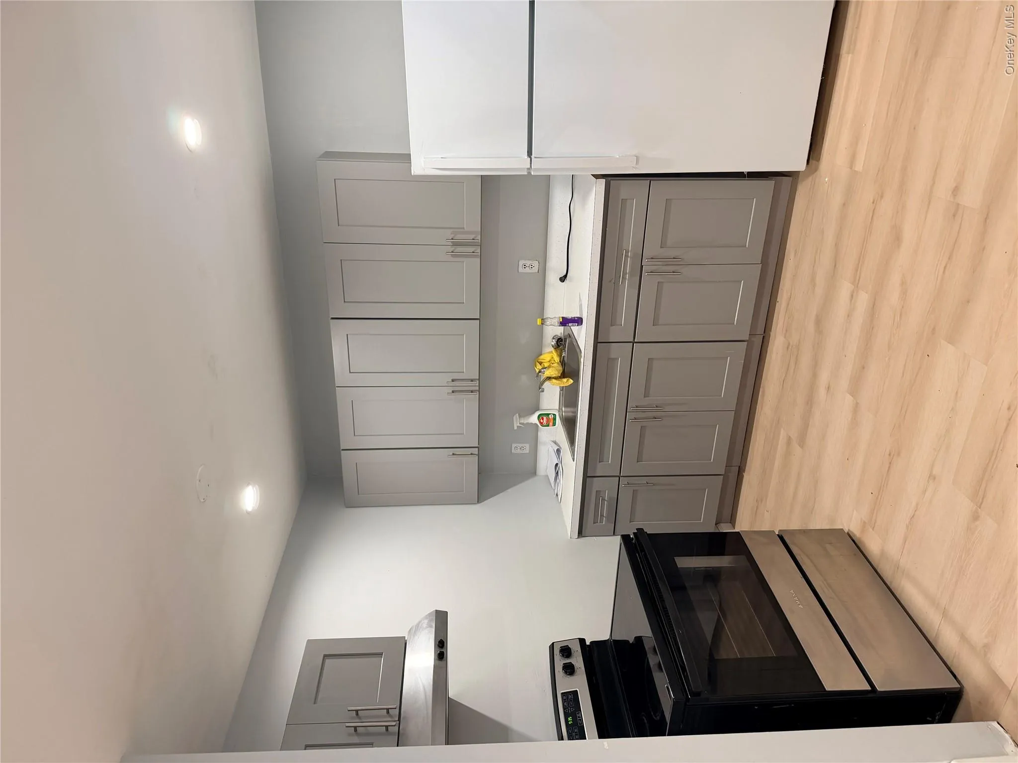 Kitchen featuring gray shaker-style cabinetry, solid-surface countertops, recessed lighting, and wood-finish flooring Kitchen featuring gray shaker-style cabinetry, solid-surface countertops, recessed lighting, and wood-finish flooring