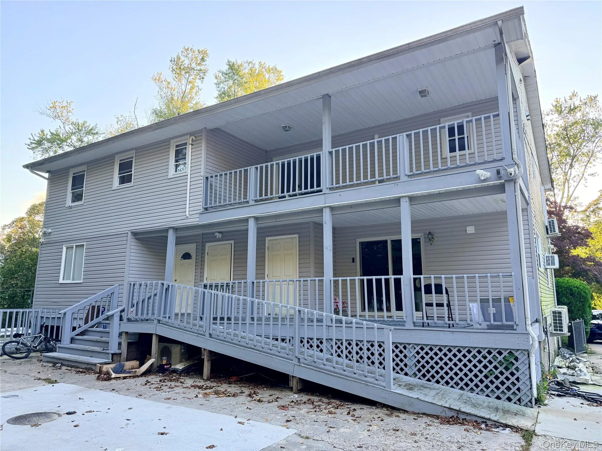 Two-story exterior featuring light gray vinyl siding, a full-length covered porch, a second-level balcony with railings, and an integrated wood-frame access ramp Two-story exterior featuring light gray vinyl siding, a full-length covered porch, a second-level balcony with railings, and an integrated wood-frame access ramp