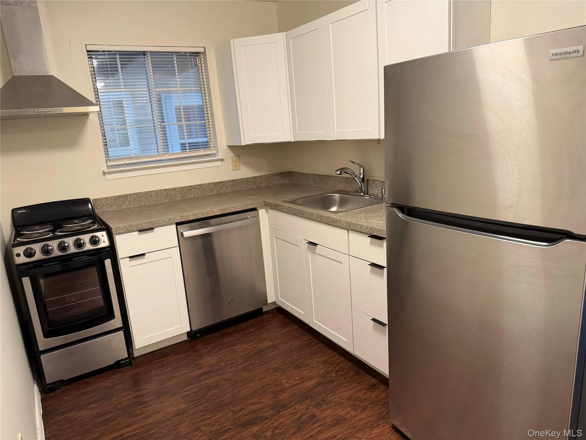 Kitchen featuring stainless steel appliances, white cabinetry, a stainless steel sink, and wood-finish flooring. Kitchen featuring stainless steel appliances, white cabinetry, a stainless steel sink, and wood-finish flooring.