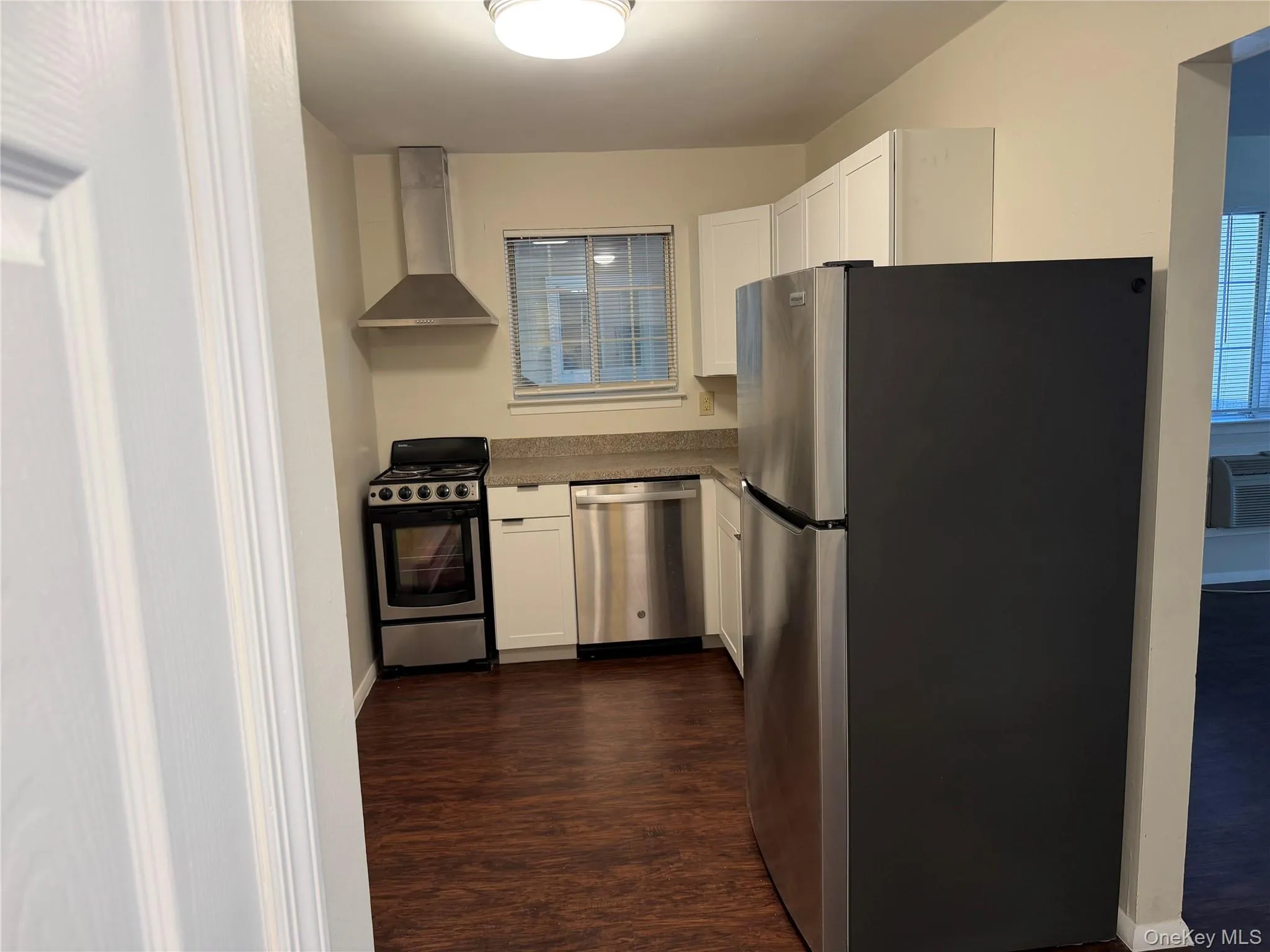 Kitchen featuring wood-finish flooring, white cabinetry, a stainless steel range hood, stainless steel dishwasher, and a stainless steel refrigerator. Kitchen featuring wood-finish flooring, white cabinetry, a stainless steel range hood, stainless steel dishwasher, and a stainless steel refrigerator.