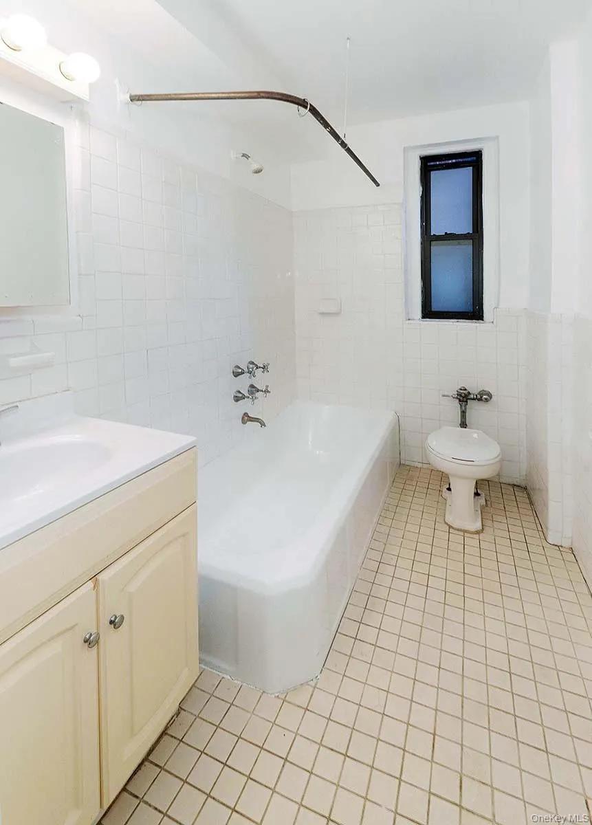 Bathroom featuring a white vanity cabinet with a integrated sink, bathtub with a chrome faucet and shower head, wall-mounted ceramic tile, and a privacy window Bathroom featuring a white vanity cabinet with a integrated sink, bathtub with a chrome faucet and shower head, wall-mounted ceramic tile, and a privacy window