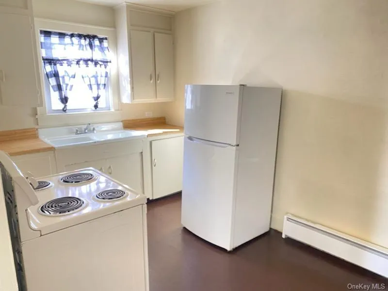 Kitchen featuring a white built-in sink, upper and lower cabinetry, white freestanding refrigerator, and a white freestanding electric range Kitchen featuring a white built-in sink, upper and lower cabinetry, white freestanding refrigerator, and a white freestanding electric range