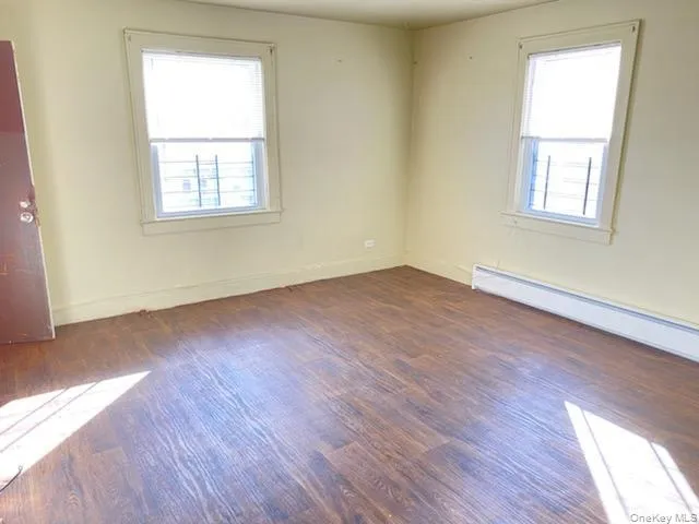 Room with wood-finish flooring, two windows, and a baseboard heating unit Room with wood-finish flooring, two windows, and a baseboard heating unit