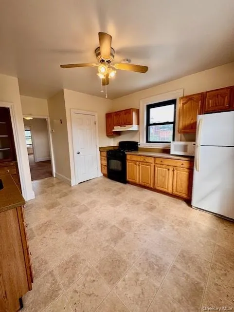 Kitchen featuring white appliances, under cabinet range hood, a ceiling fan, and plenty of natural light Kitchen featuring white appliances, under cabinet range hood, a ceiling fan, and plenty of natural light
