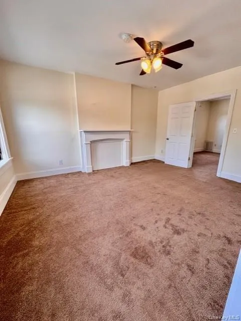 Unfurnished living room with a ceiling fan, carpet flooring, and a fireplace Unfurnished living room with a ceiling fan, carpet flooring, and a fireplace