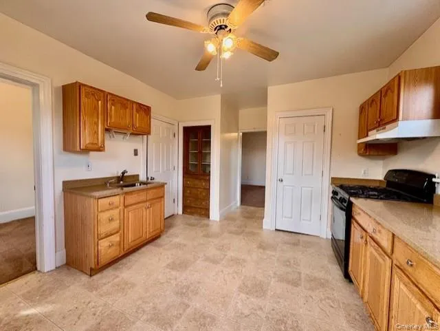 Kitchen with black range with gas stovetop, under cabinet range hood, ceiling fan, and brown cabinets Kitchen with black range with gas stovetop, under cabinet range hood, ceiling fan, and brown cabinets
