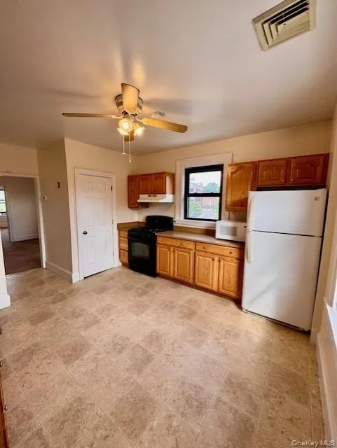 Kitchen featuring white appliances, under cabinet range hood, plenty of natural light, and brown cabinetry Kitchen featuring white appliances, under cabinet range hood, plenty of natural light, and brown cabinetry