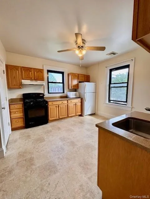Kitchen featuring white appliances, under cabinet range hood, plenty of natural light, and brown cabinets Kitchen featuring white appliances, under cabinet range hood, plenty of natural light, and brown cabinets