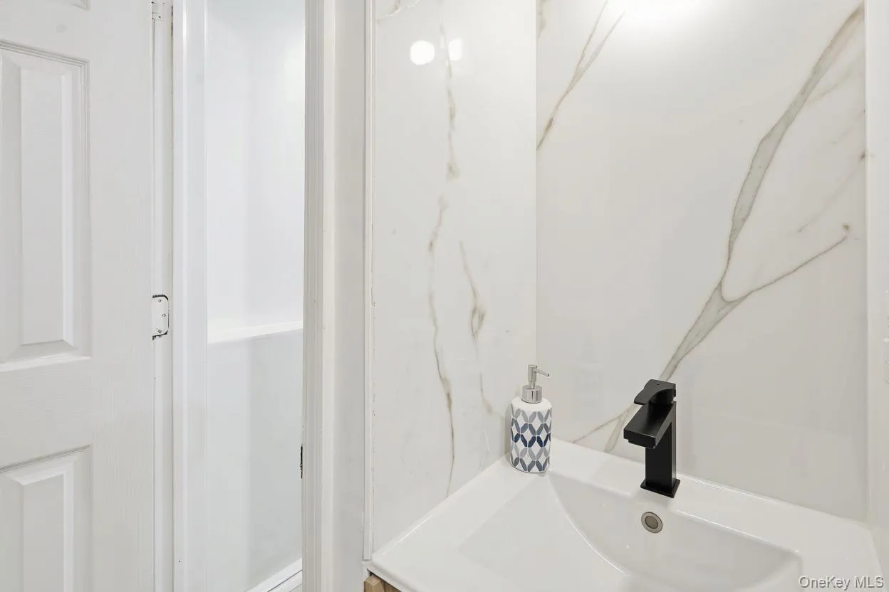 Downstairs Bathroom vanity featuring large-format veined tile backsplash, white integral sink, and matte black faucet Downstairs Bathroom vanity featuring large-format veined tile backsplash, white integral sink, and matte black faucet
