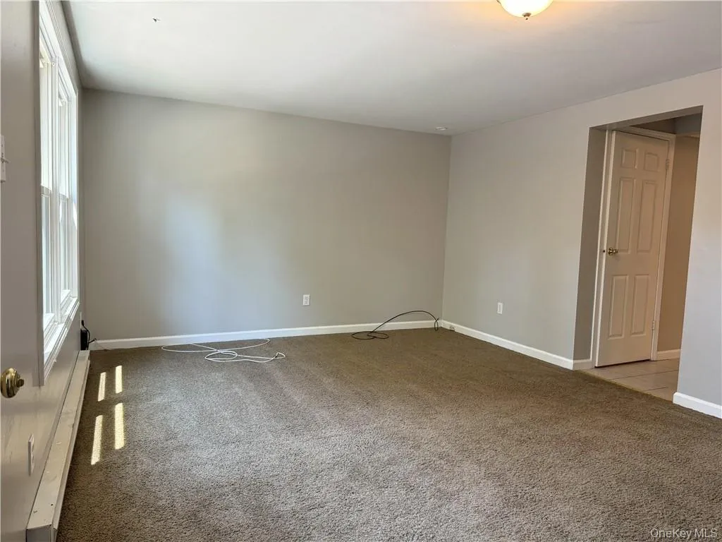 Empty room with light carpet and a baseboard radiator Empty room with light carpet and a baseboard radiator