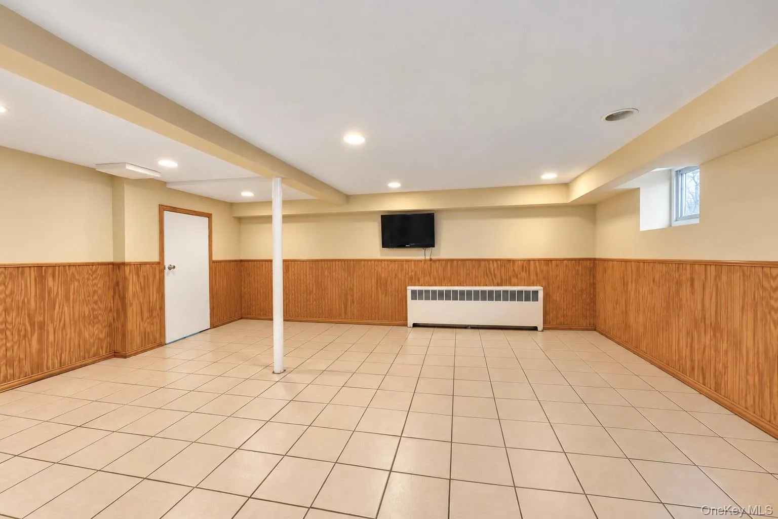 Open-concept room featuring light-colored ceramic tile flooring, wood-paneled walls, recessed ceiling lighting, and a window Open-concept room featuring light-colored ceramic tile flooring, wood-paneled walls, recessed ceiling lighting, and a window