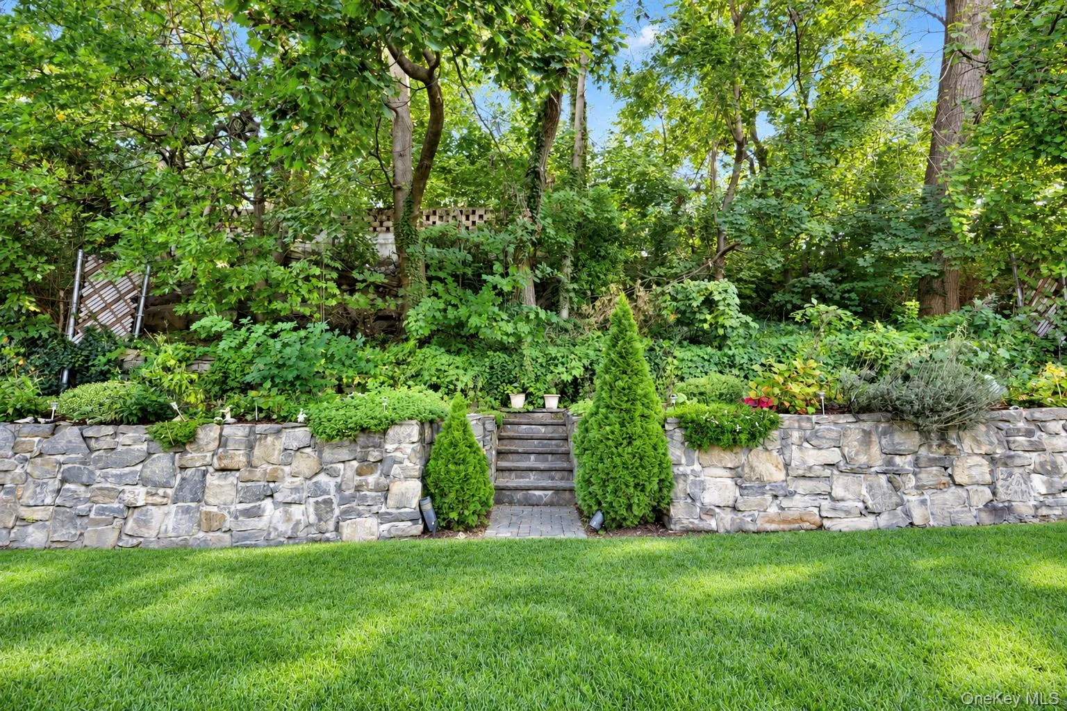 Manicured lawn, tiered natural stone retaining wall, stone staircase, and mature trees Manicured lawn, tiered natural stone retaining wall, stone staircase, and mature trees